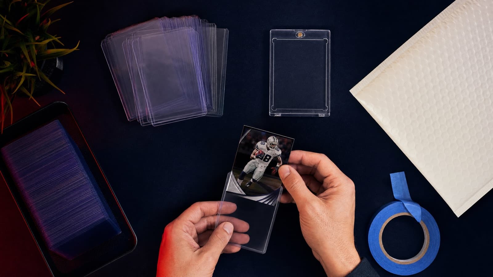 Penny sleeves, top loaders, a bubble mailer, and painter's tape arranged for shipping sports cards safely